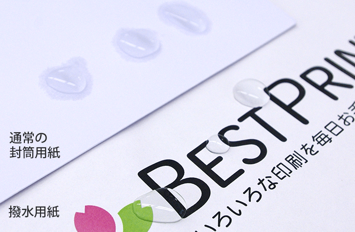 通常の封筒用紙と撥水用紙の上に水滴が乗せてから1分後の写真。通常の封筒用紙は、水分が紙に水が浸み込んでおり水滴の周りの紙の色が濃くなっている状態。封筒用紙は、水滴を乗せた直後とほぼ変わっていない。